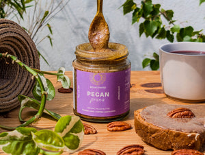 Organic Pecan Butter from 100% Bio-activated pecans, with a spoonful out, surrounded by pecans, on toast with a cup of tea.